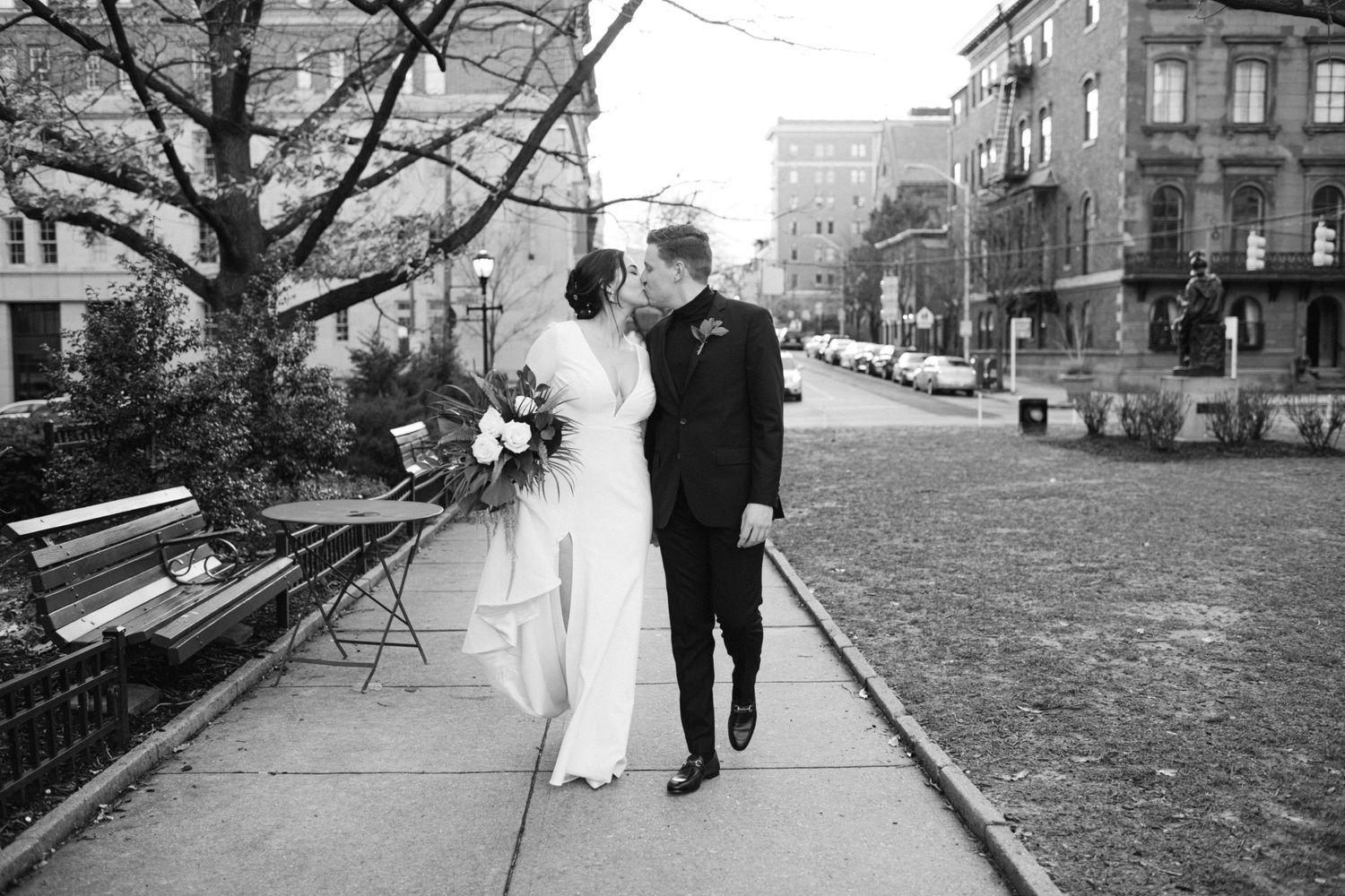 Black and white photo of newlyweds walking together on a city sidewalk.