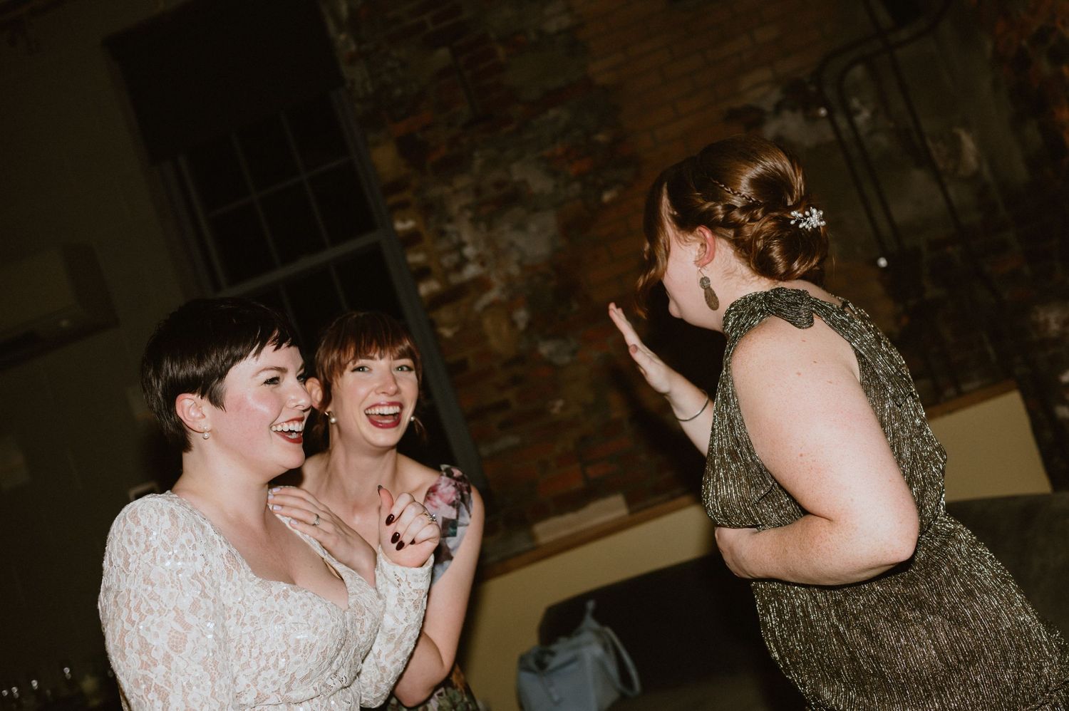 Wedding guests dancing and laughing together at a reception with exposed brick walls.