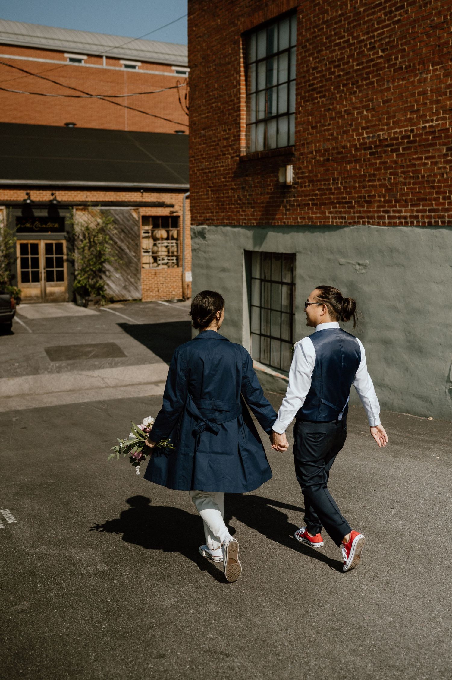 A couple holding hands walks through an urban alley in coordinated blue and white outfits.