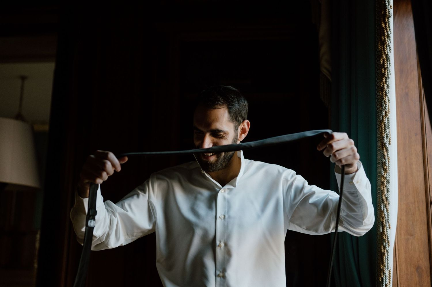 Person in white clothing holding a dark fabric or belt against dramatic shadows.