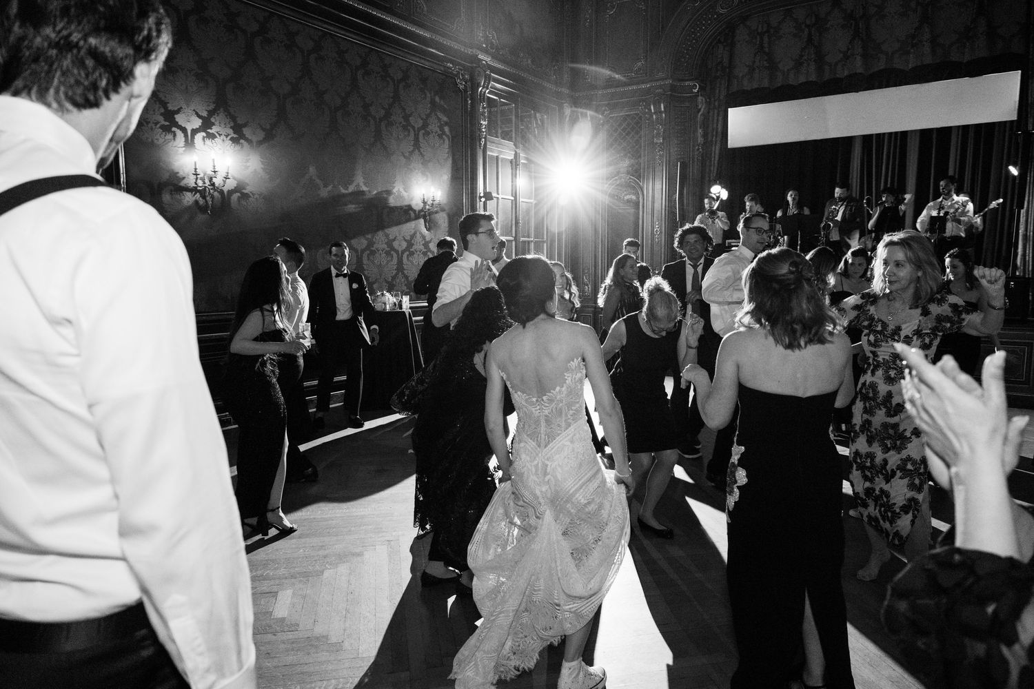 Black and white photo of wedding guests dancing and celebrating on a dimly lit dance floor.