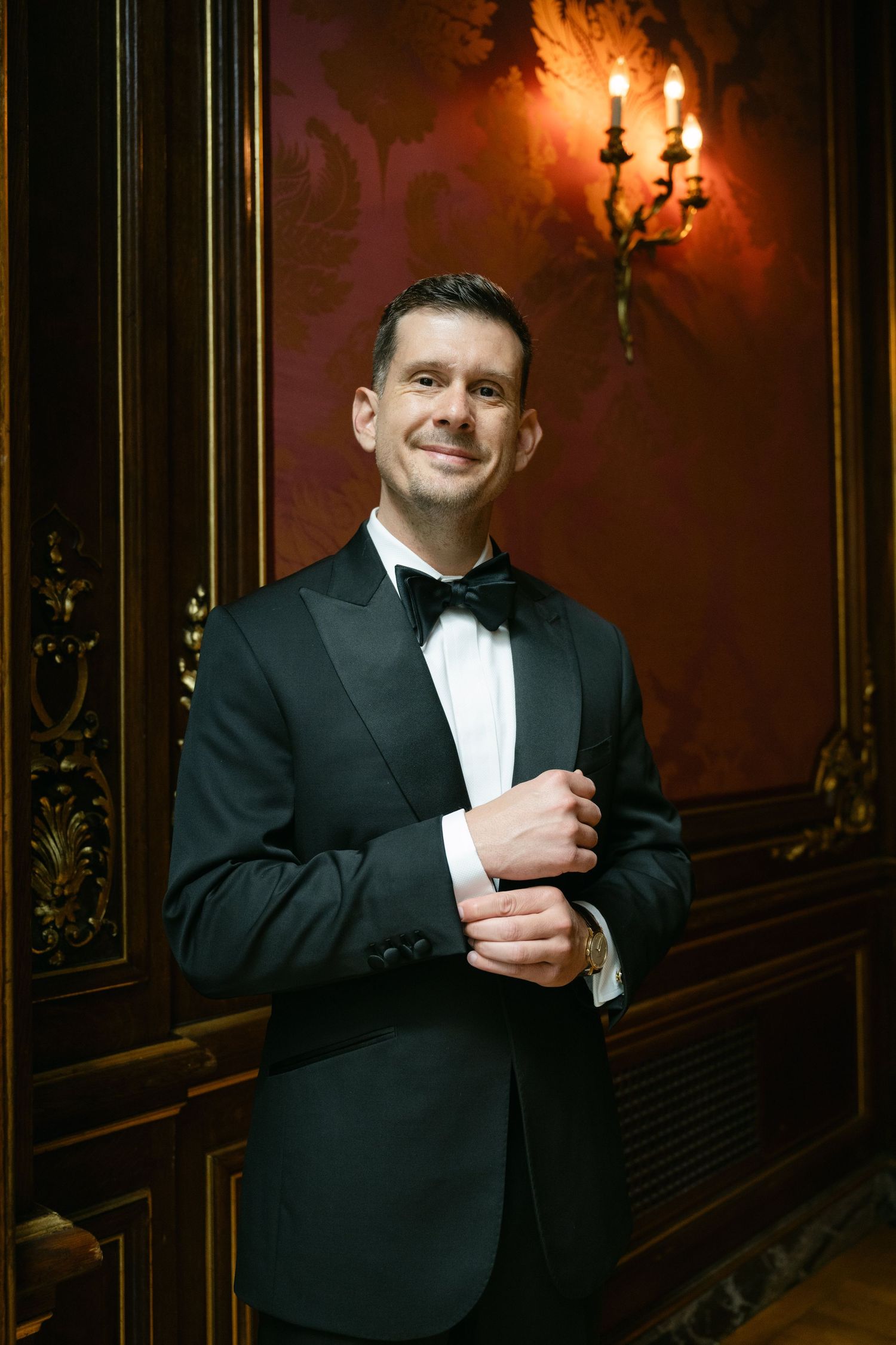 A formal portrait in a luxurious room with dark wood paneling and golden wall sconces.