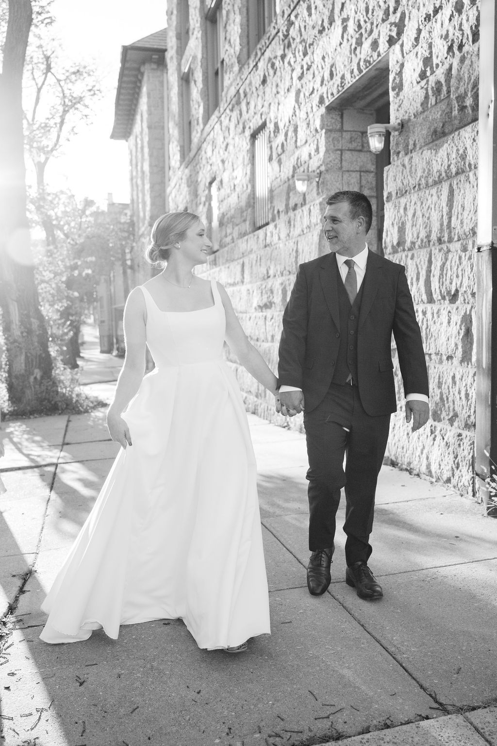 A sunlit wedding portrait against a stone wall backdrop on a bright afternoon.