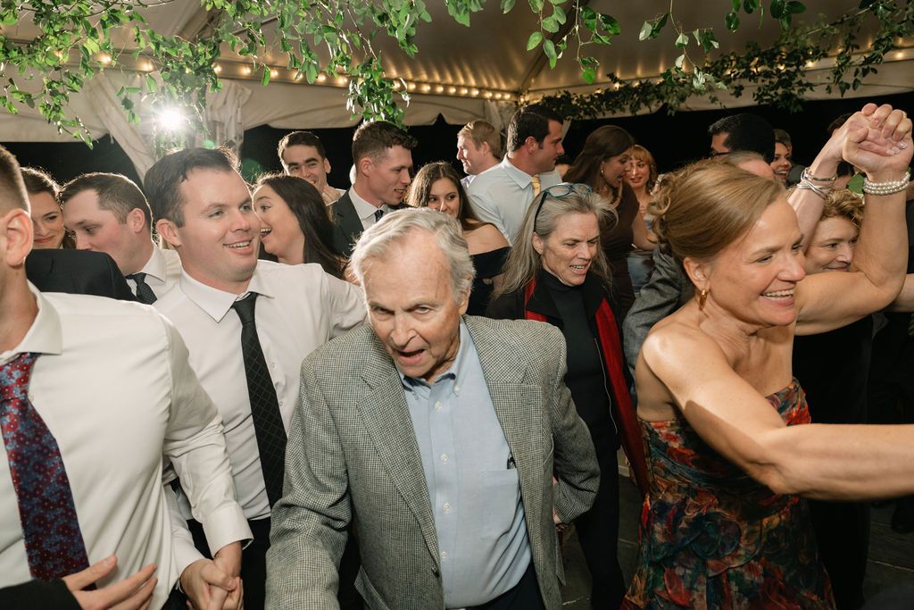 Energetic dancing and celebration on a crowded reception dance floor with string lights overhead.