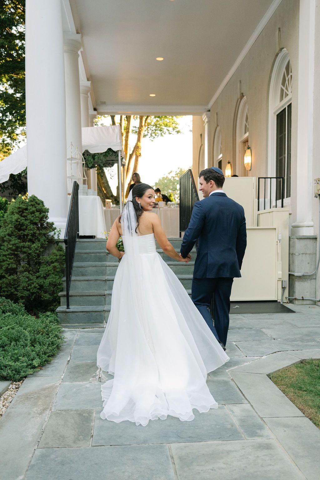 Wedding couple walking along a white columned porch of an elegant building at Strong Mansion on Sugarloaf Mountain