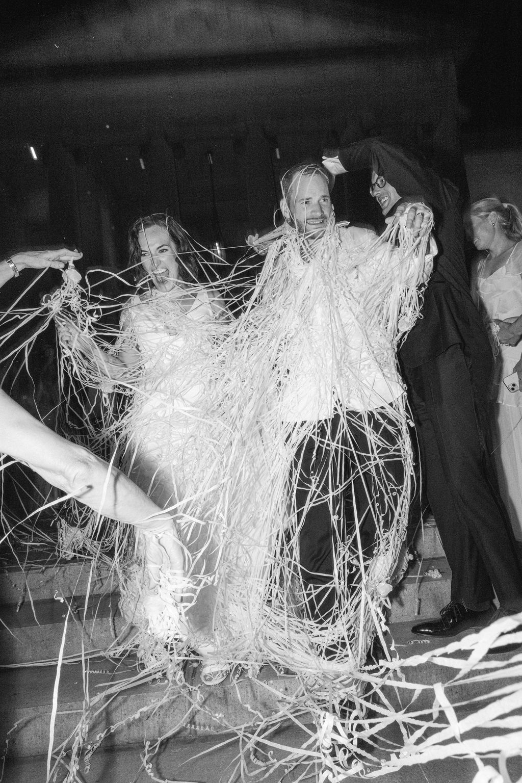 Black and white photo sequence showing people wrapped in swirling white streamers during a performance or art installation.