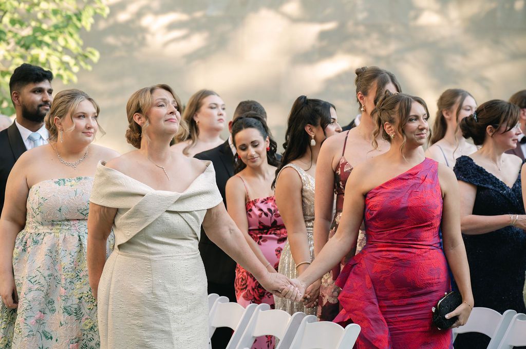 Wedding guests in formal attire gather outdoors at an elegant celebration, wearing colorful dresses and suits.