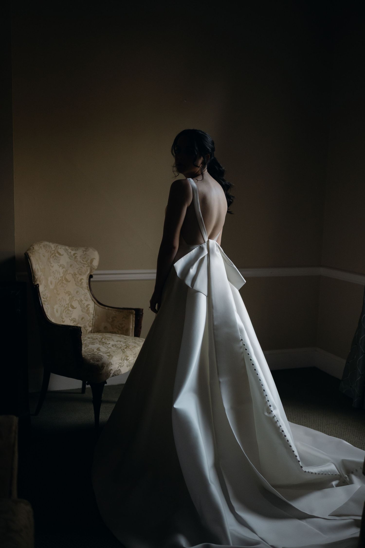 Dramatic lighting captures the silhouette of a wedding dress in a minimalist room setting.