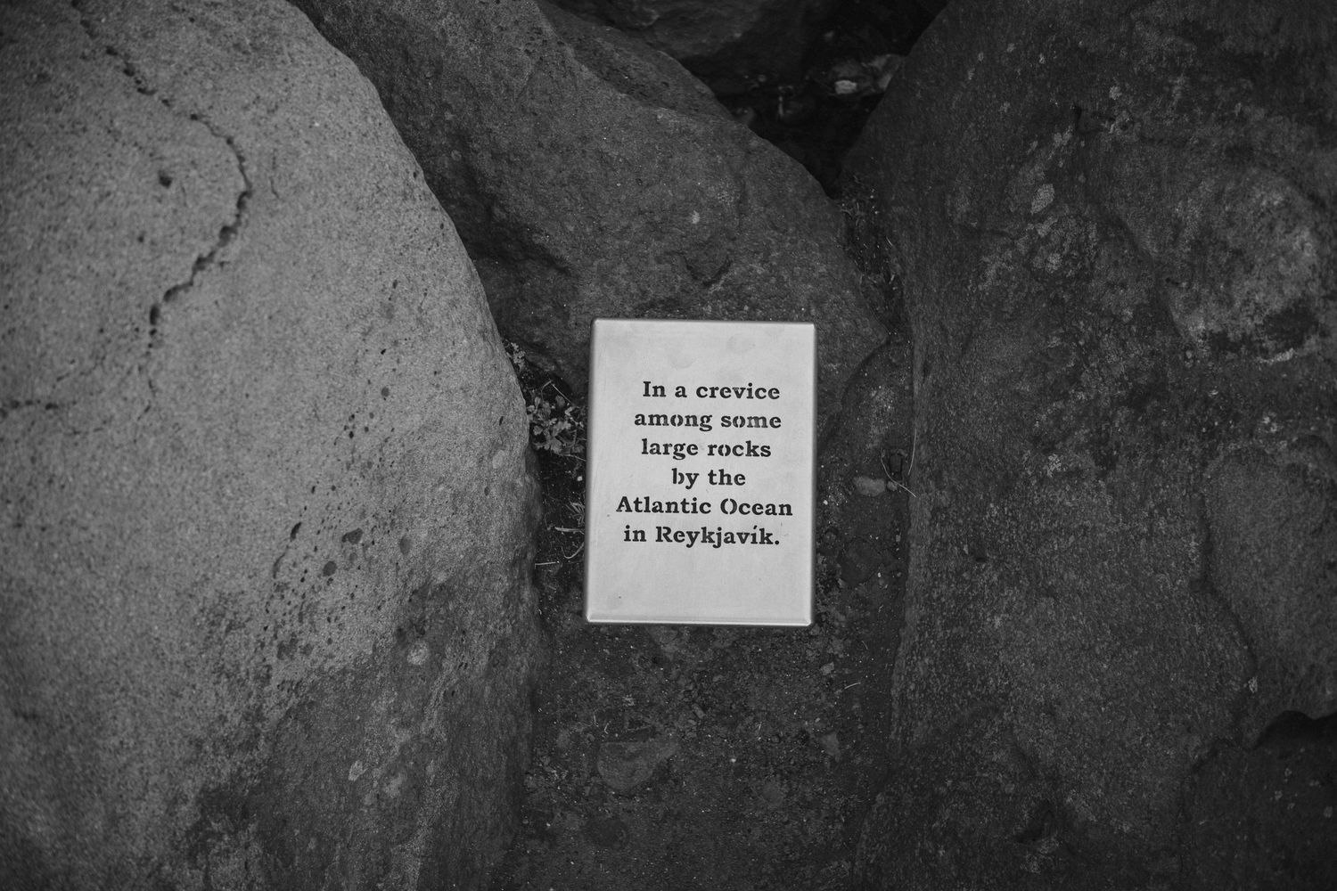 Black and white photograph of a small sign mounted between rocks.
