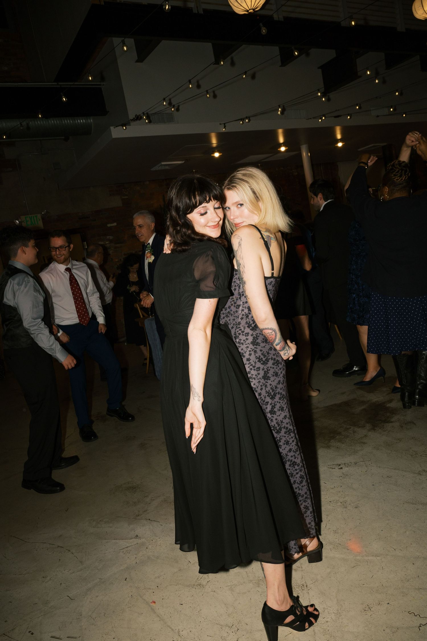 Two guests in evening wear share an intimate dance moment at a dimly lit reception.