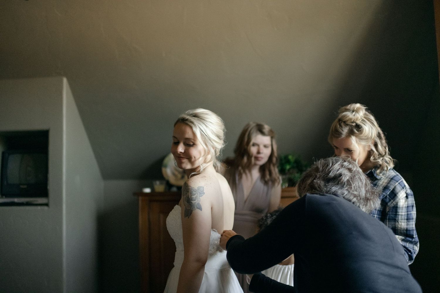 Final wedding dress preparations taking place in intimate indoor setting.