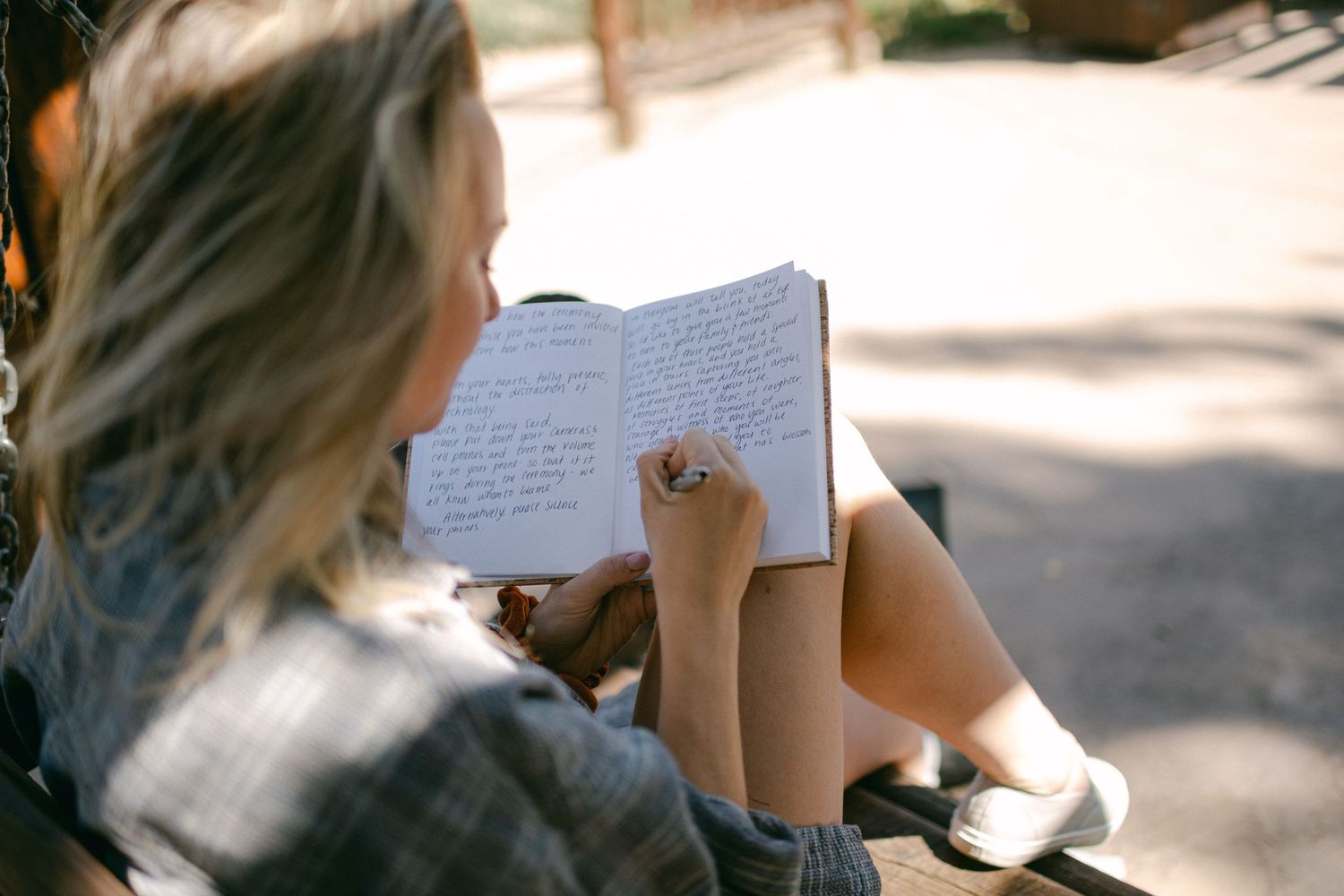 Person writing in journal while sitting outdoors in natural lighting.