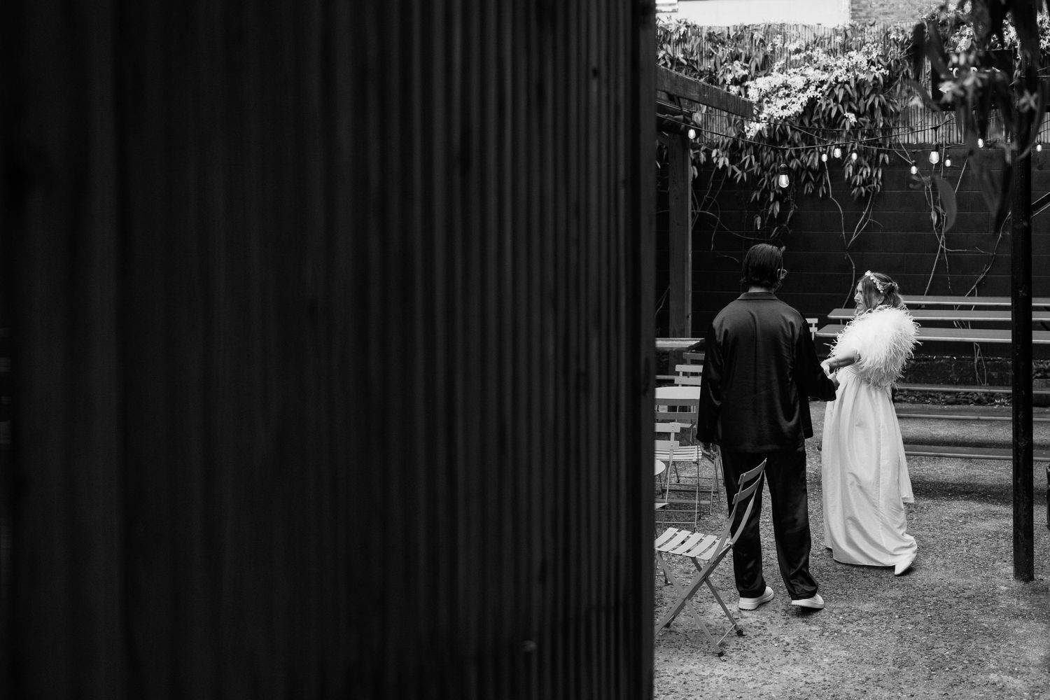 A black and white artistic photograph of a couple on their wedding day framed by a dark vertical element.