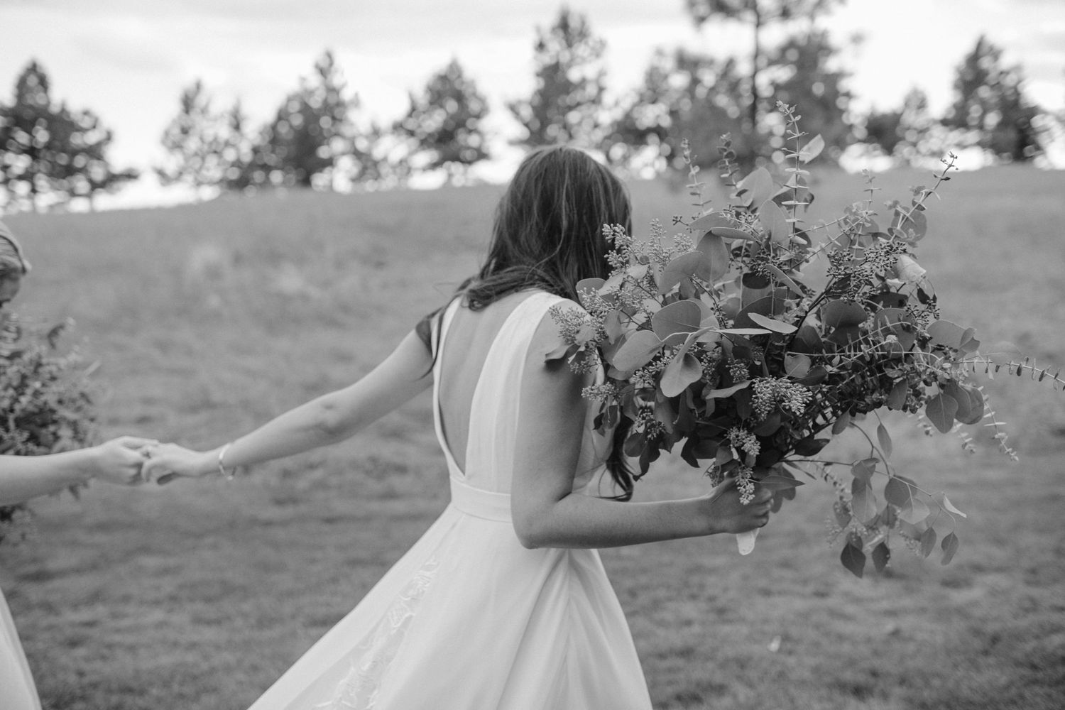 Black and white image of someone in a wedding dress twirling with a bouquet on a hillside.