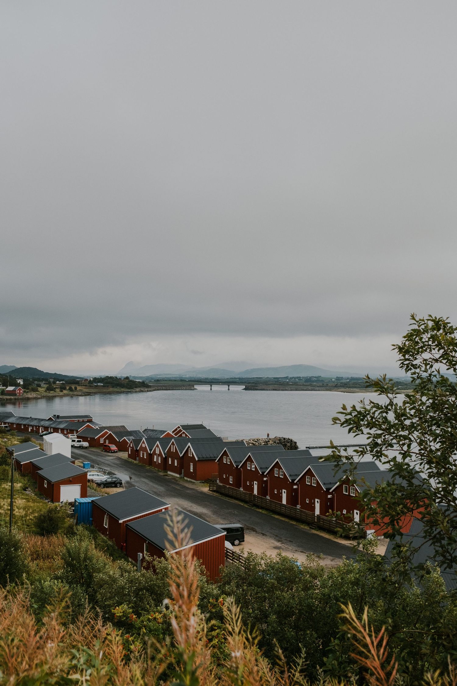 Row of red waterfront houses along Norwegian fjord under cloudy skies.