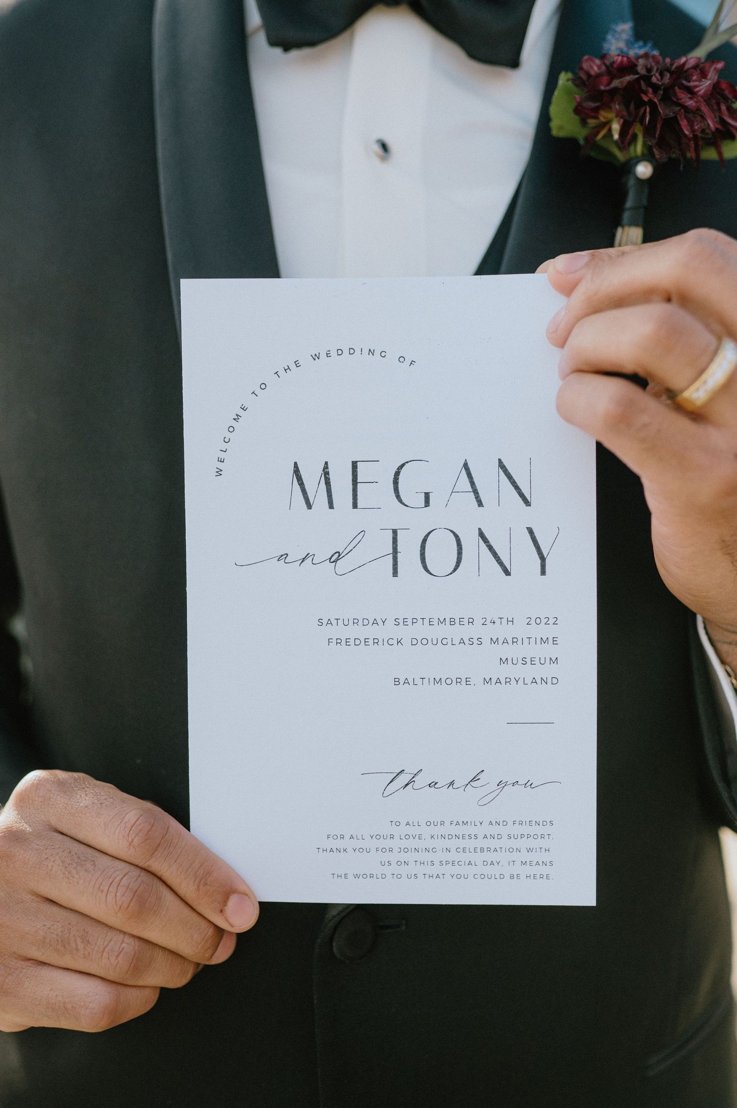Wedding invitation in minimalist design held against formal black tuxedo.