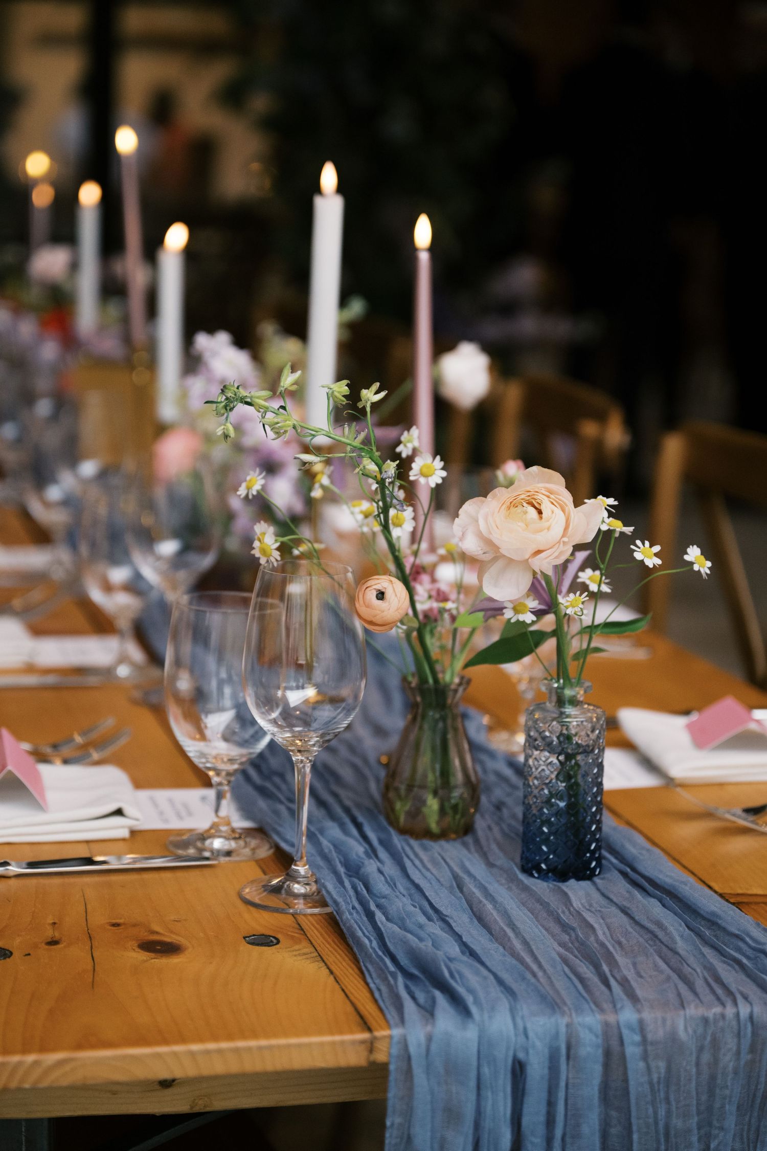 Romantic table setting with blue runner, white candles, and delicate floral centerpieces in glass vases.