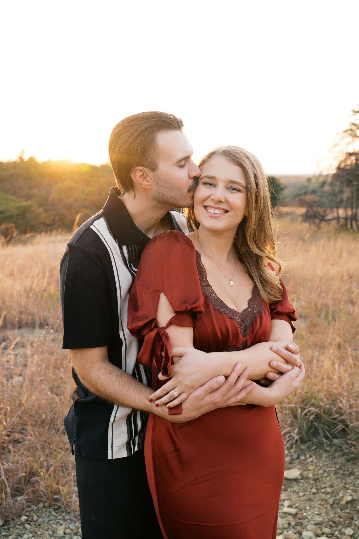 A romantic couple embraces in a golden field during sunset, sharing an intimate moment together.