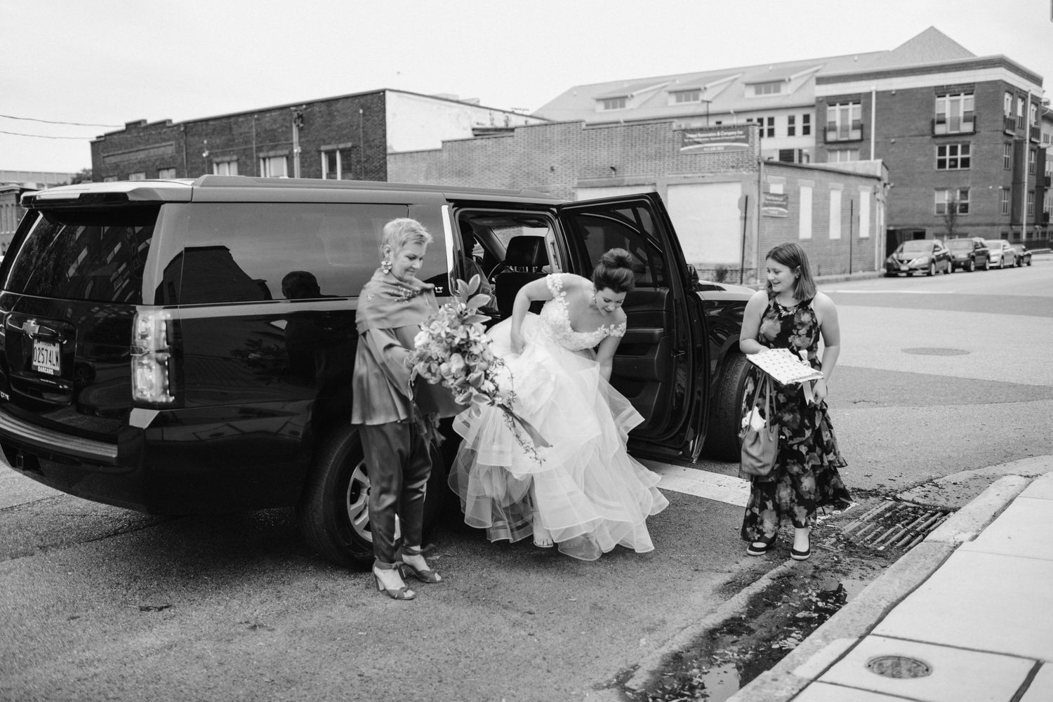 Black and white photo of attendees helping with transportation arrangements by a black SUV.