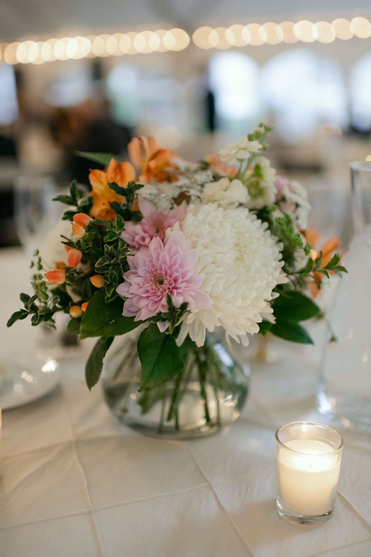 Elegant floral centerpiece with white chrysanthemums, pink dahlias, and orange lilies in a glass vase.