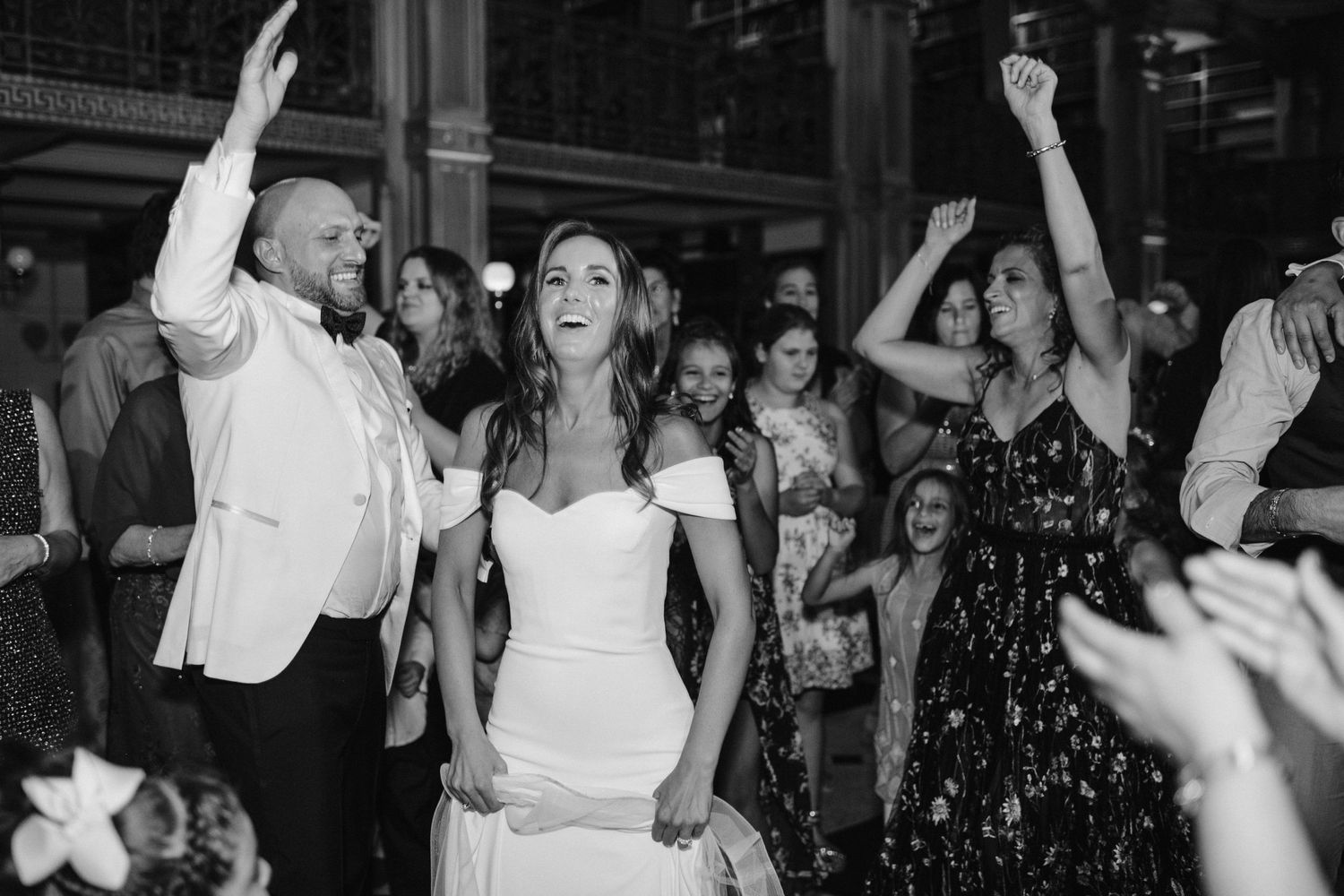 Black and white photo of guests dancing and celebrating at an elegant indoor wedding reception.