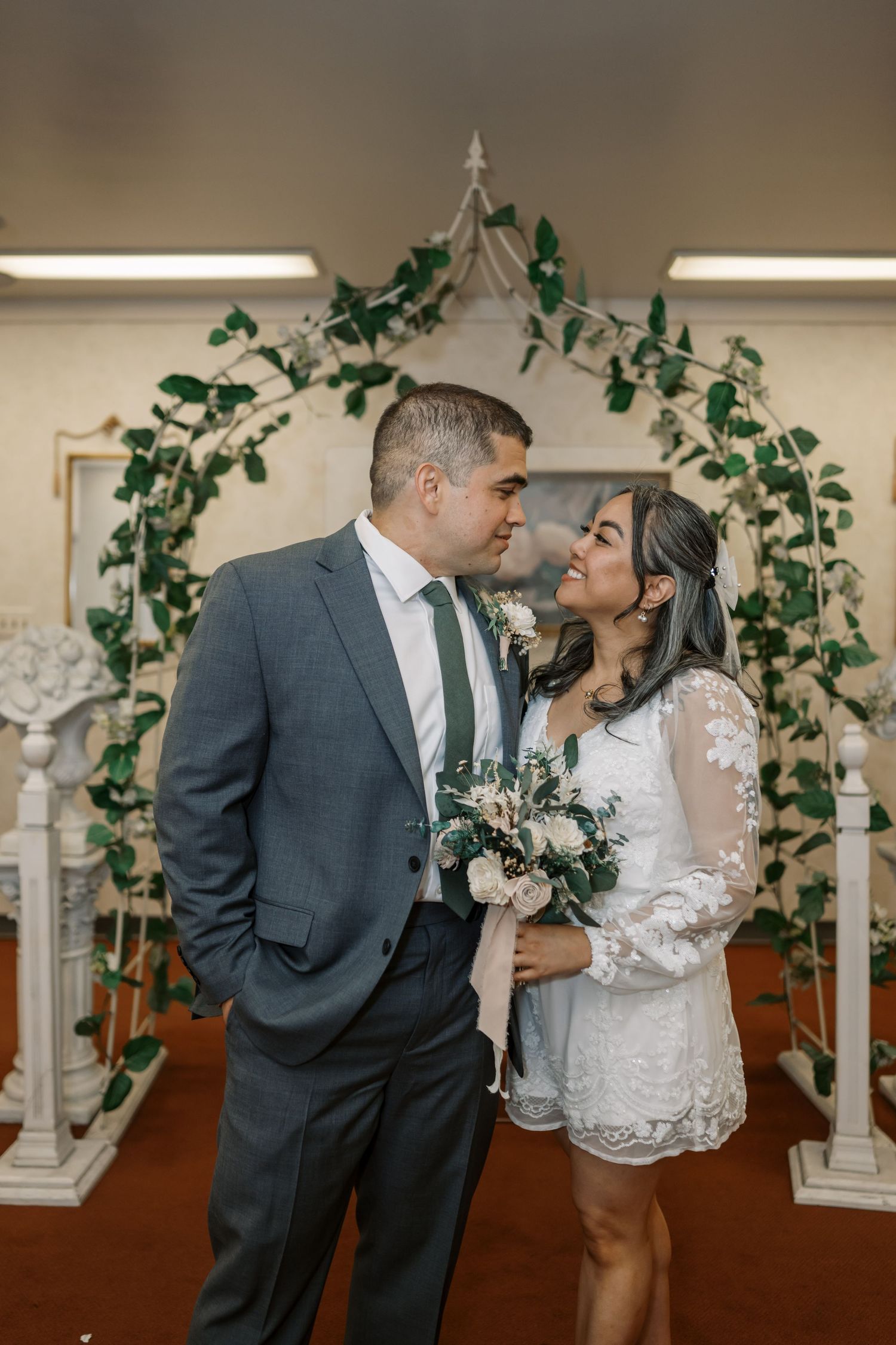Newlyweds stand under a greenery arch in a wedding chapel with classic decor.