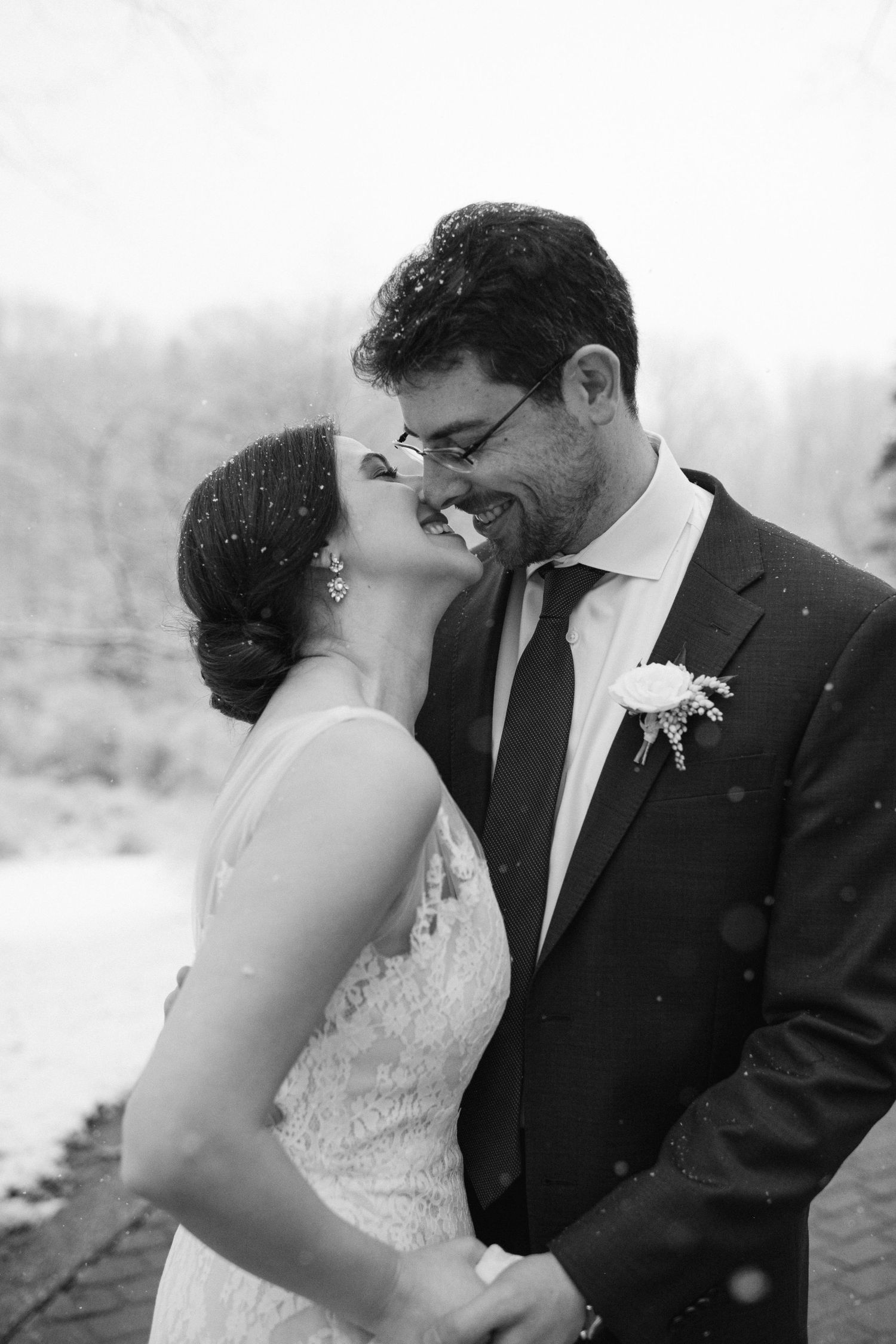 A black and white wedding portrait captures an intimate moment between newlyweds in the snow.