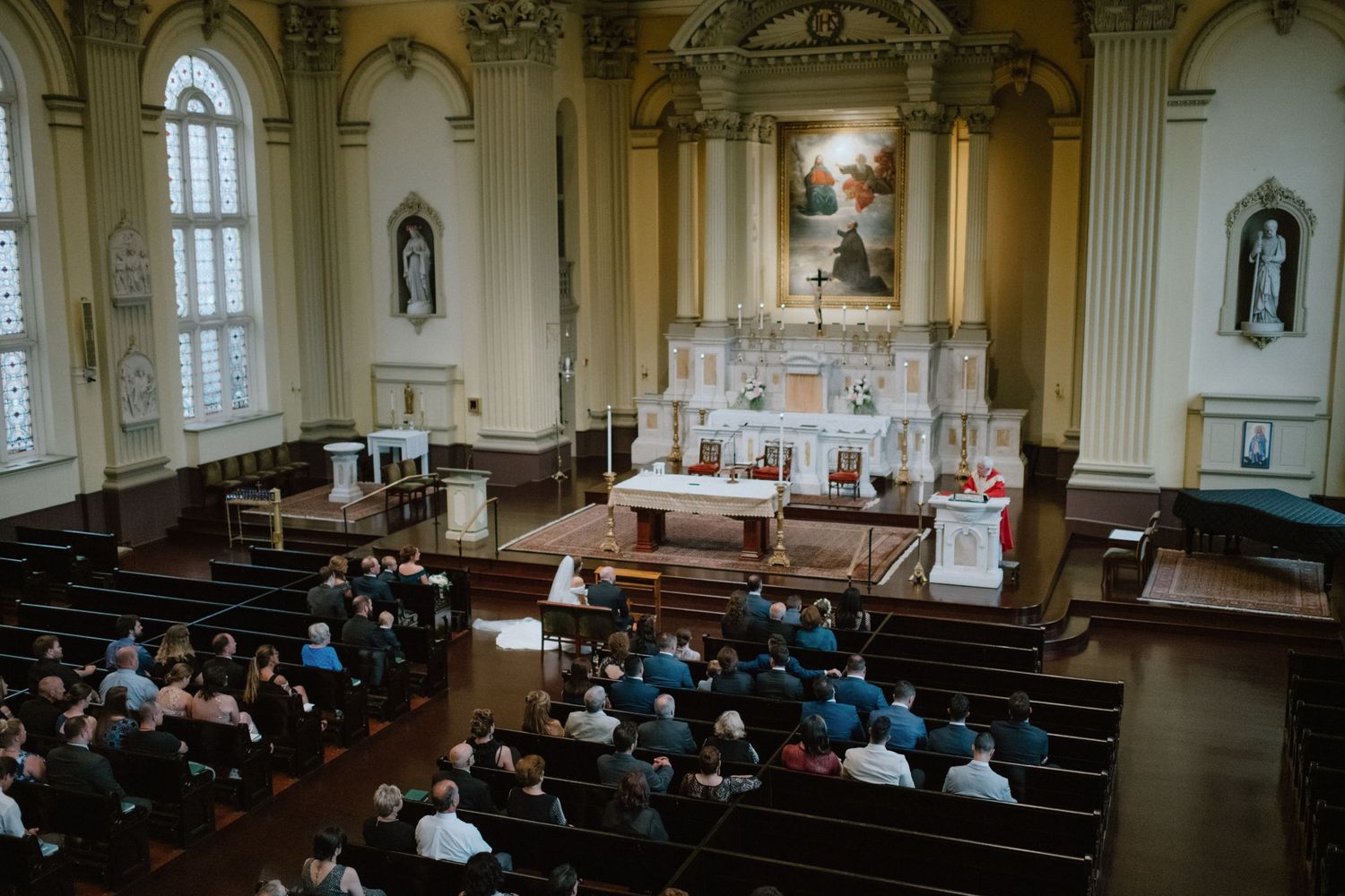 Wide shot of wedding ceremony in historic church with traditional altar and wooden pews.