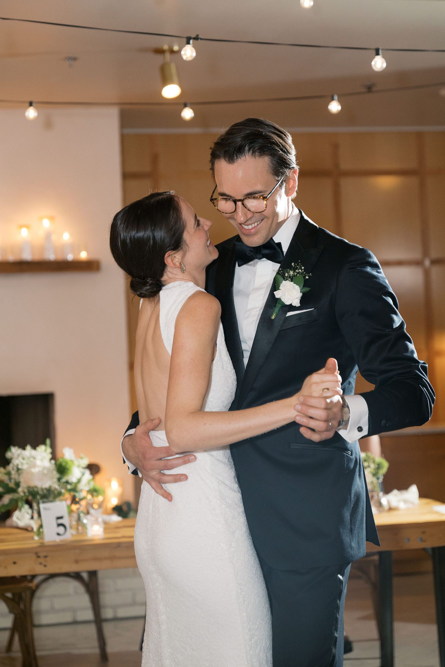 A romantic first dance between newlyweds in formal attire under soft lighting at their wedding reception.
