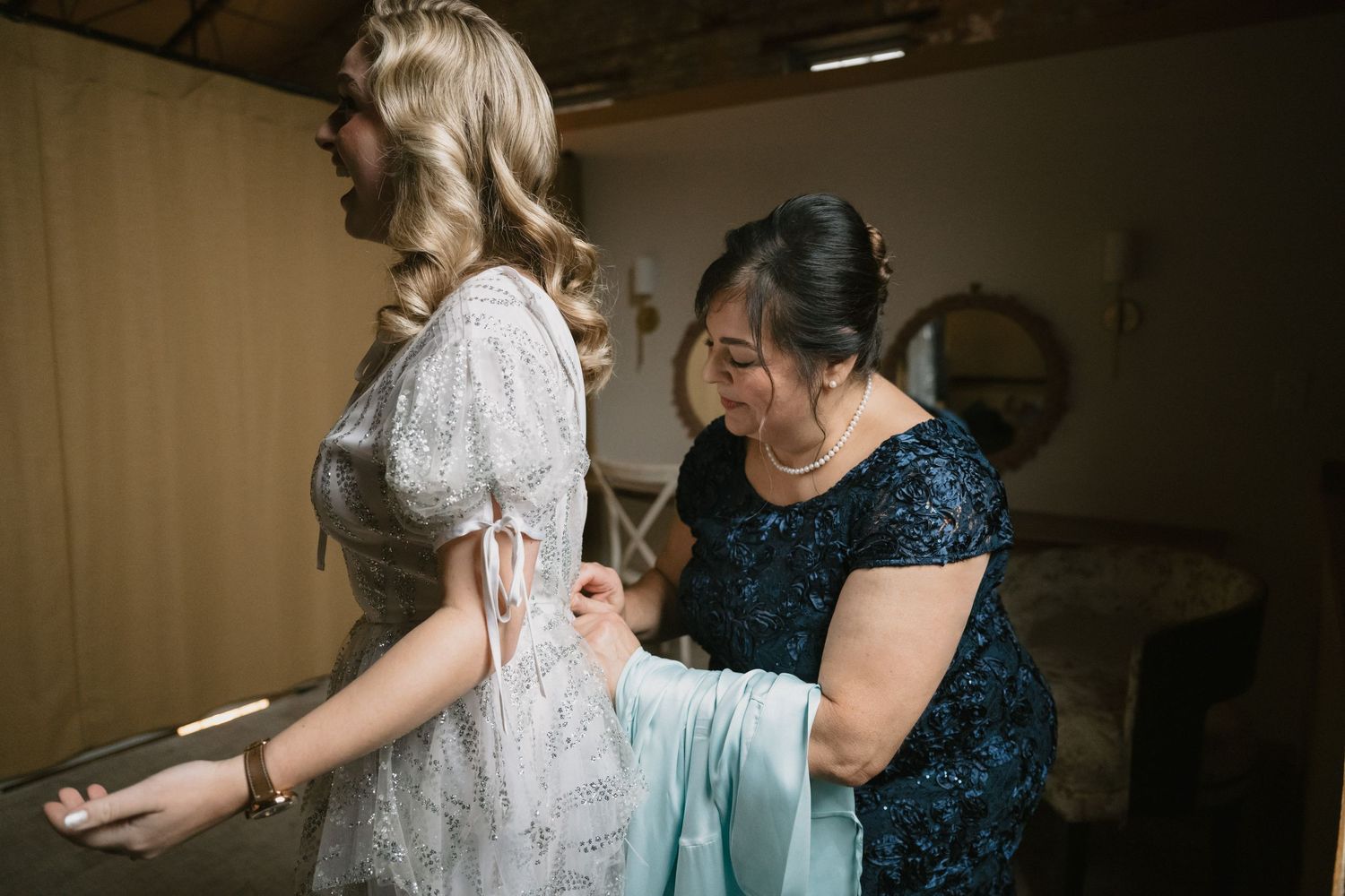 Final dress adjustments being made during wedding preparations in a rustic room.