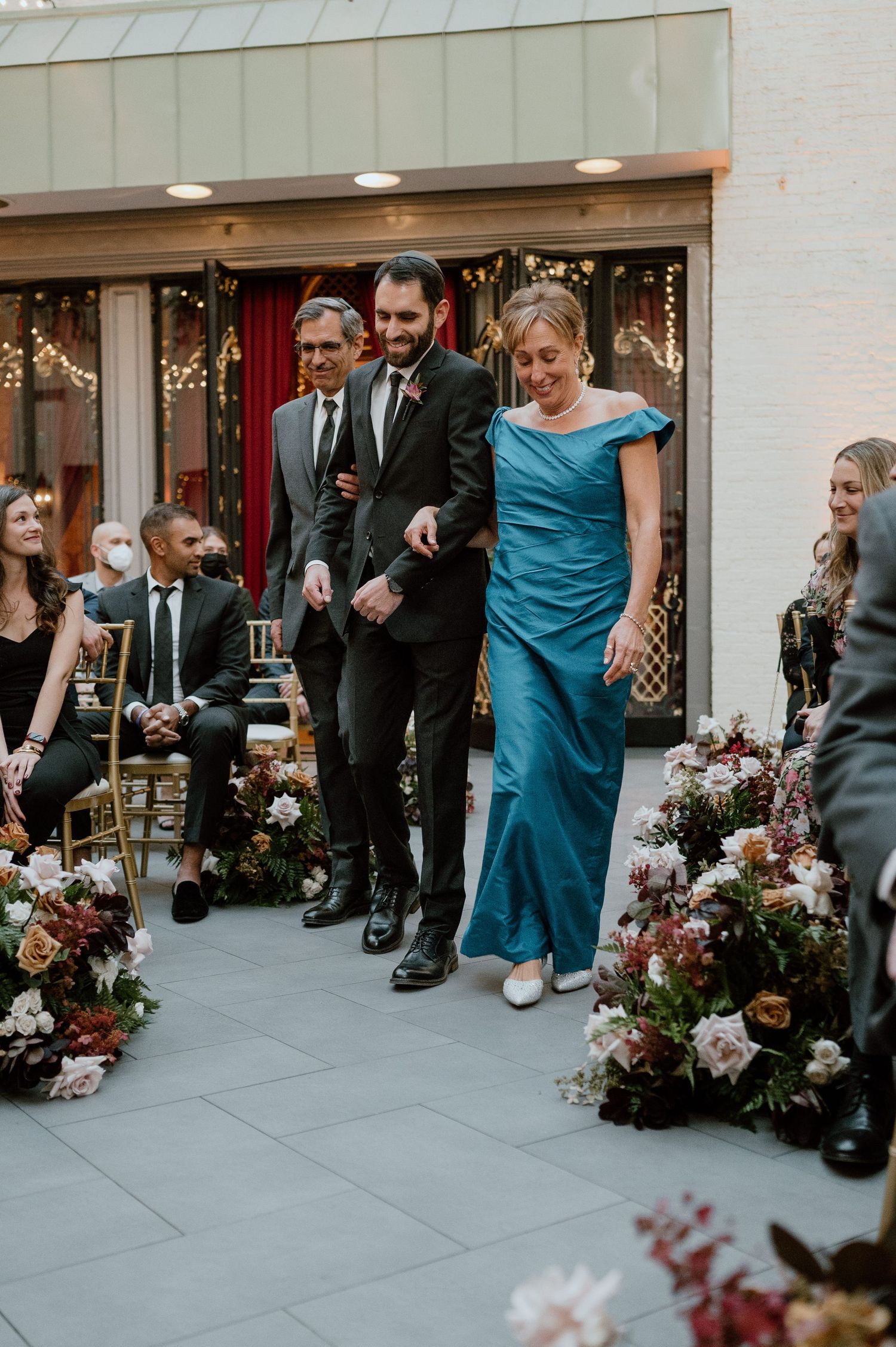 Wedding processional with attendants walking down an aisle decorated with floral arrangements.