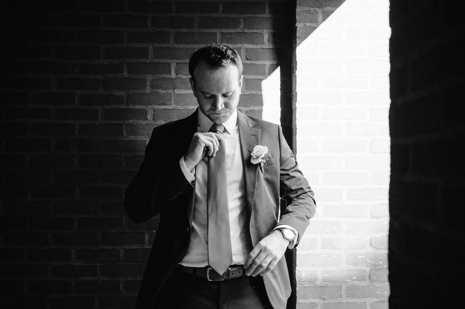 Moody black and white image of a suited figure adjusting tie in window light.