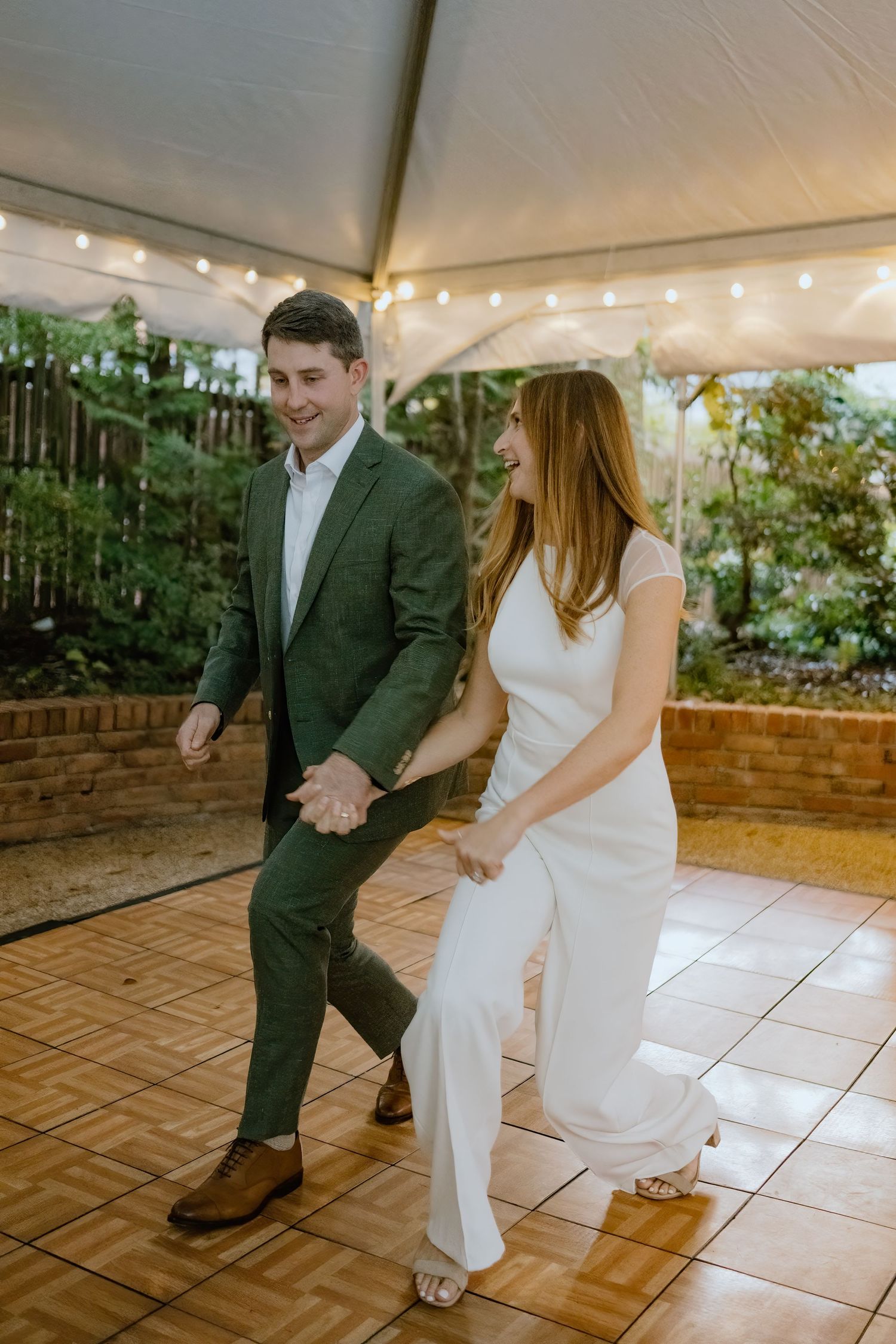 Couple performing choreographed dance moves on wooden dance floor under tent.