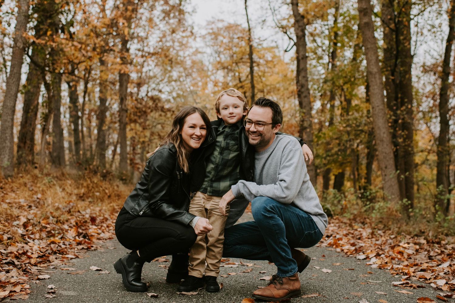 A family and their dog pose together on a fall trail surrounded by orange leaves.