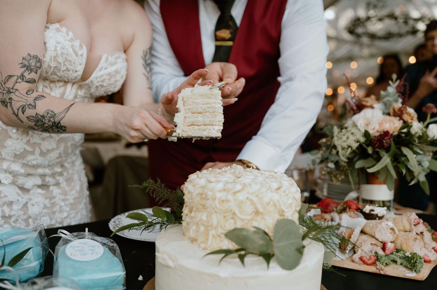 Close-up of couple cutting their elegant white wedding cake decorated with greenery.