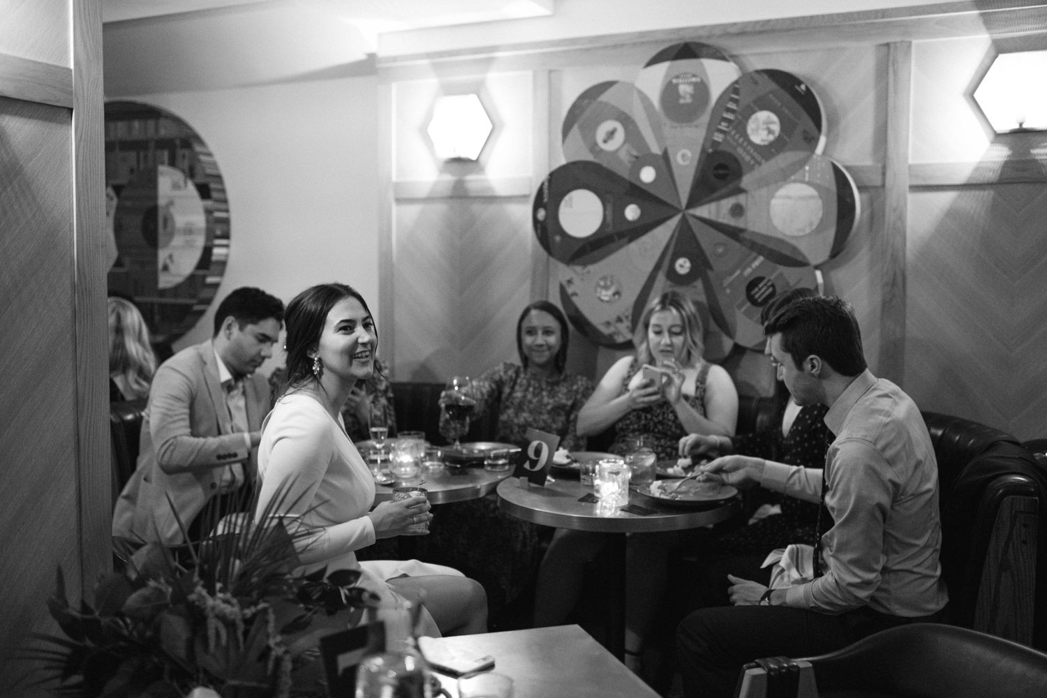 A black and white photo of friends gathering at a restaurant booth with drinks and conversation.
