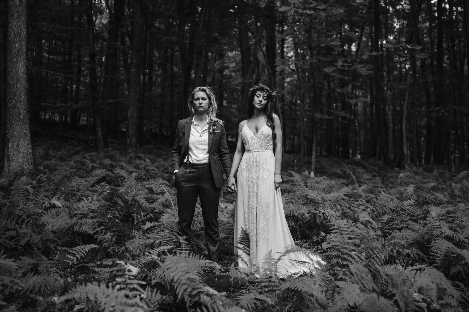 A dramatic black and white wedding portrait among lush ferns in a forest setting.