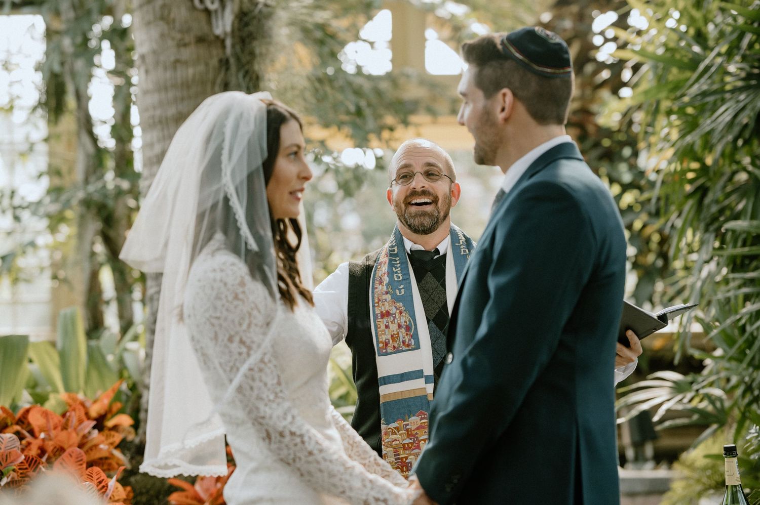 A couple shares joyful laughter with their officiant during their greenhouse wedding ceremony.