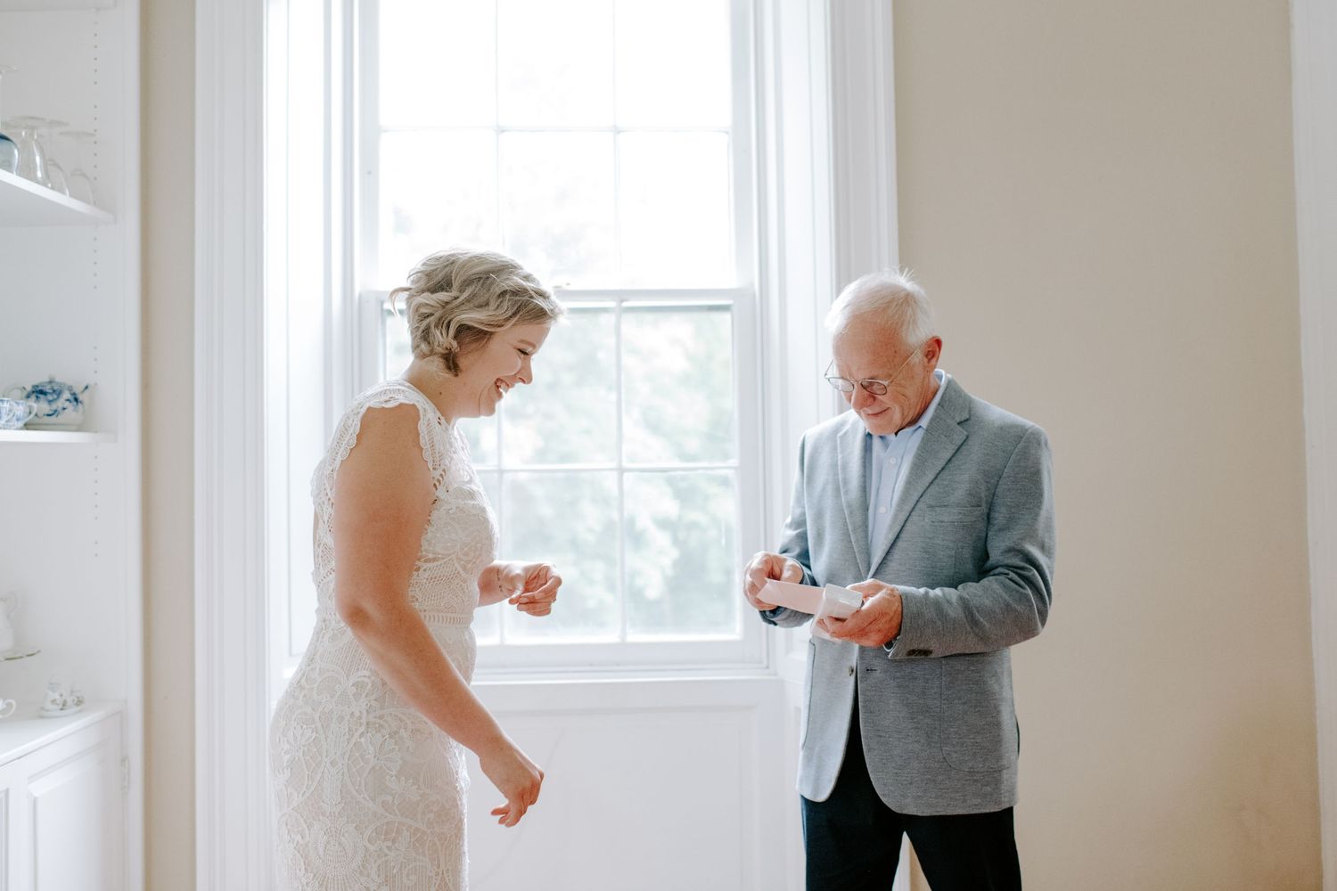 Two people share a candid interaction in a bright, minimalist room with large windows.
