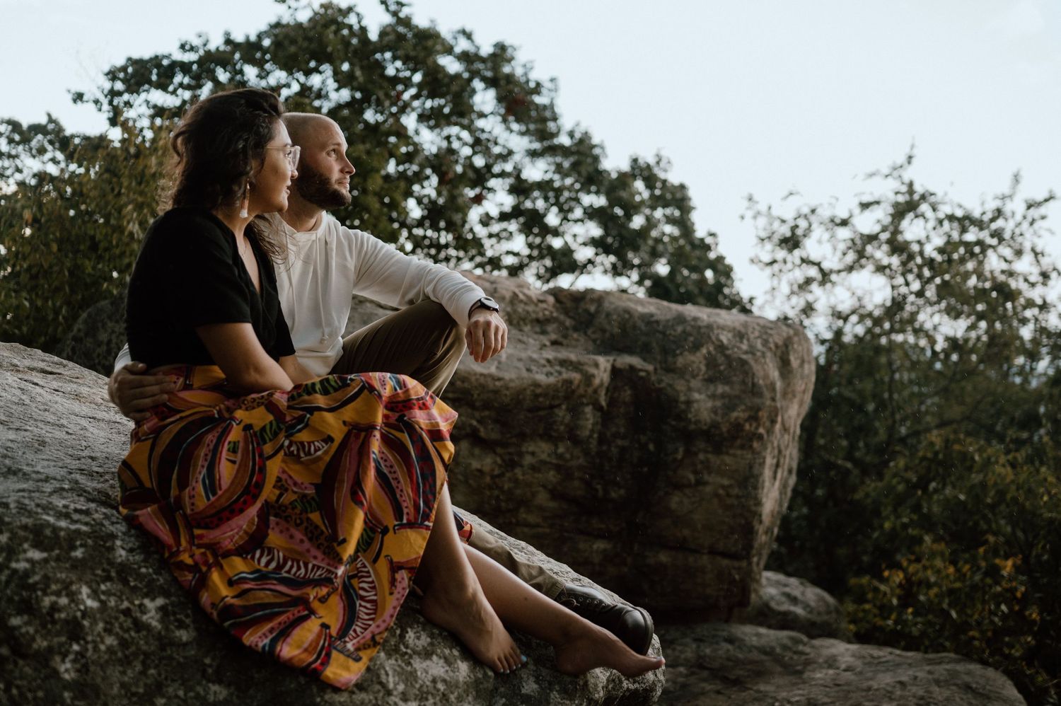 A couple in casual clothes sitting together on a rocky outcrop during golden hour.