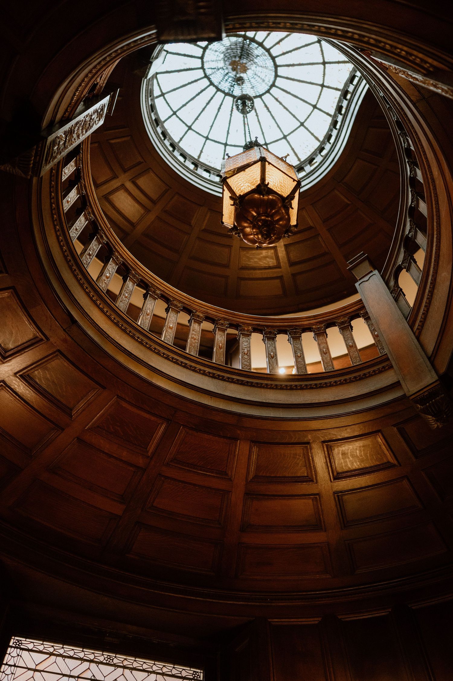 Looking up at an elegant domed rotunda with wooden panels and a glass skylight ceiling.