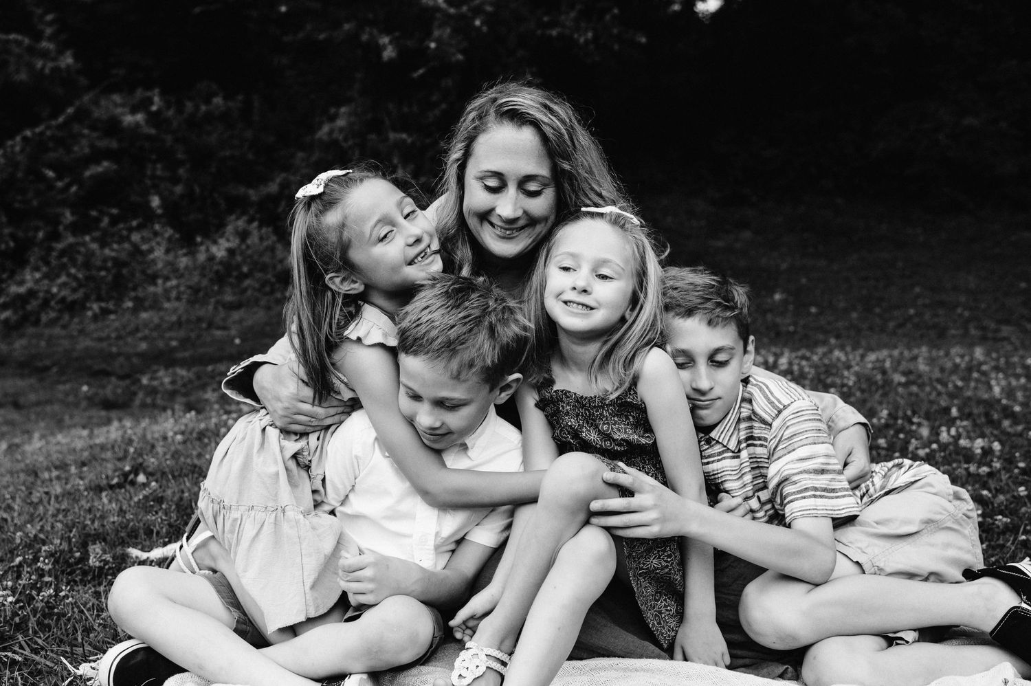 A joyful family cuddle session captured in black and white photography on a grassy hillside.