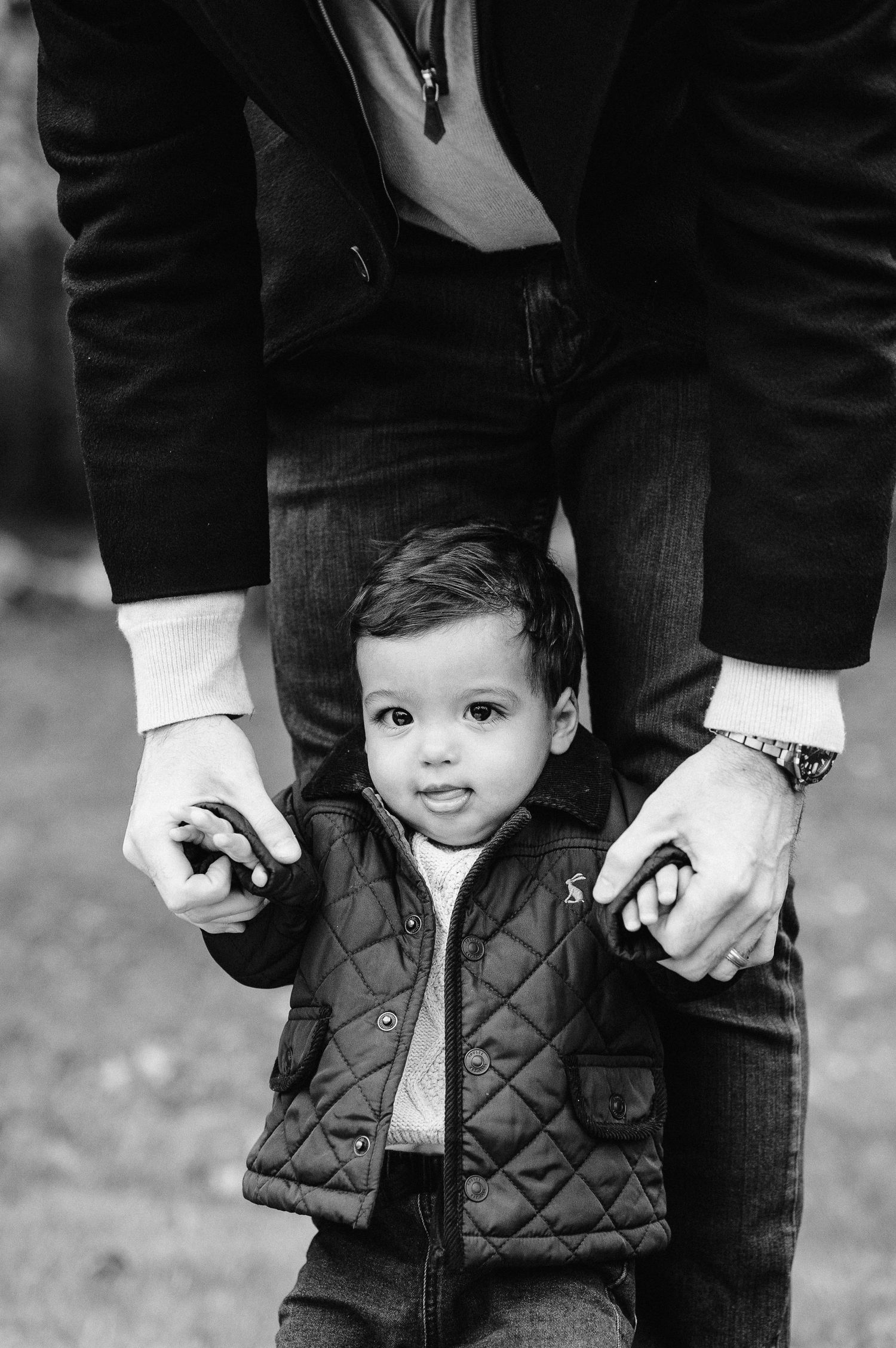 Black and white portrait of small child in quilted vest holding hands with adult.