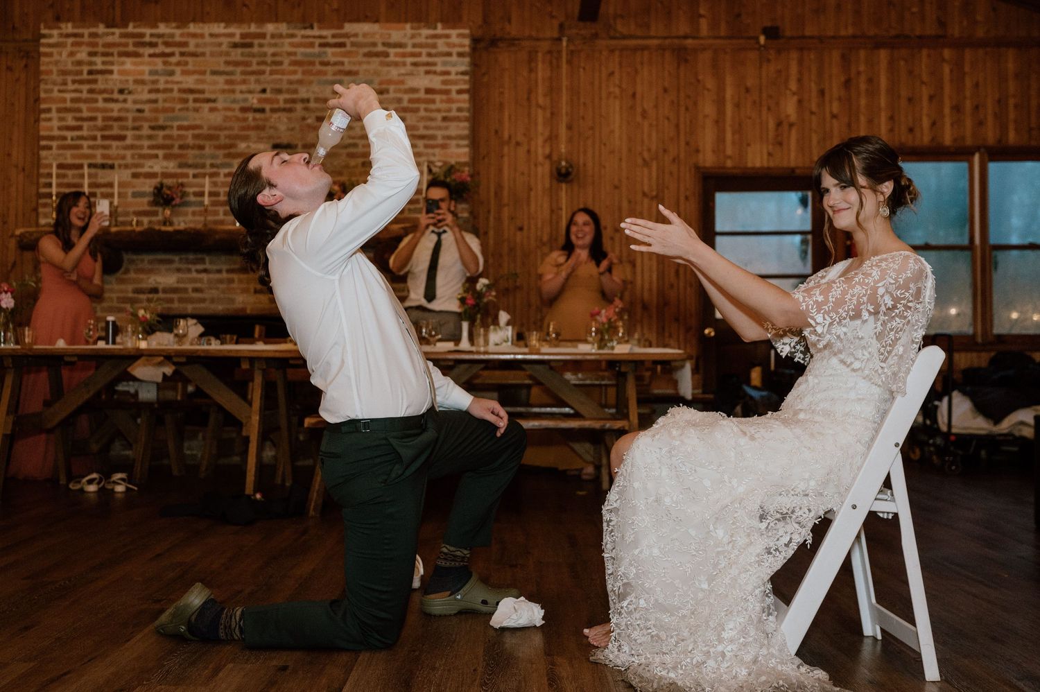 Playful wedding couple performing garter toss moment at rustic barn reception.