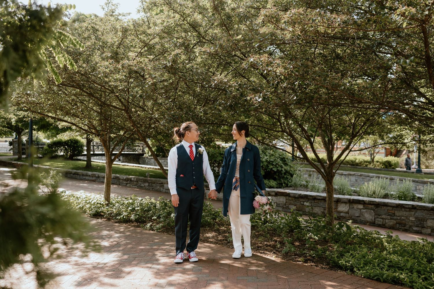 A couple walks together through a tree-lined park pathway.