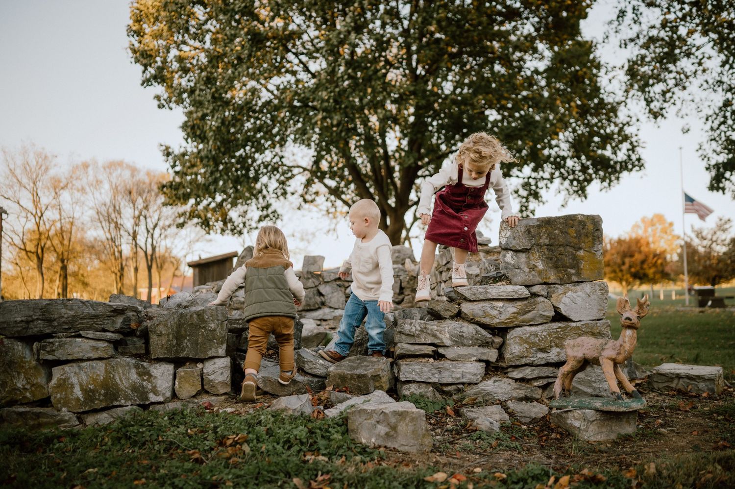 Children explore and play on a rustic stone wall during golden hour.