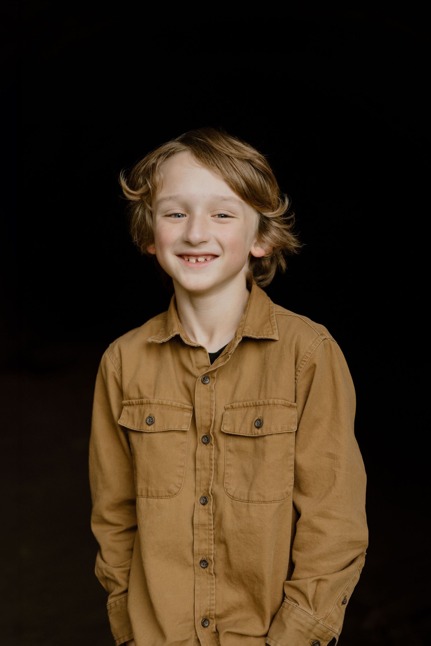 A warm portrait against dark background featuring someone in a tan button-up shirt.