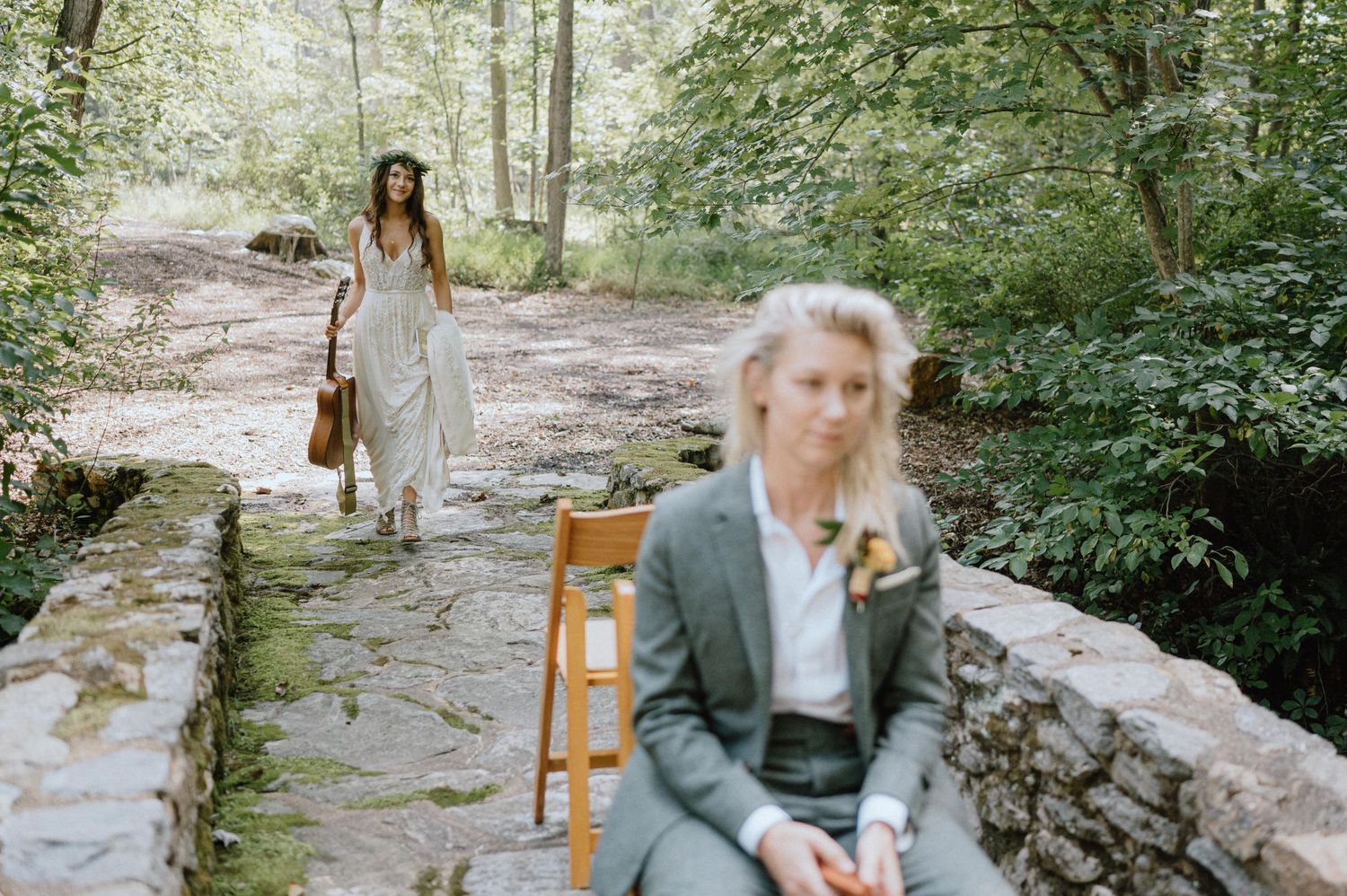 Two people in wedding attire pose separately on a stone path in a wooded setting.