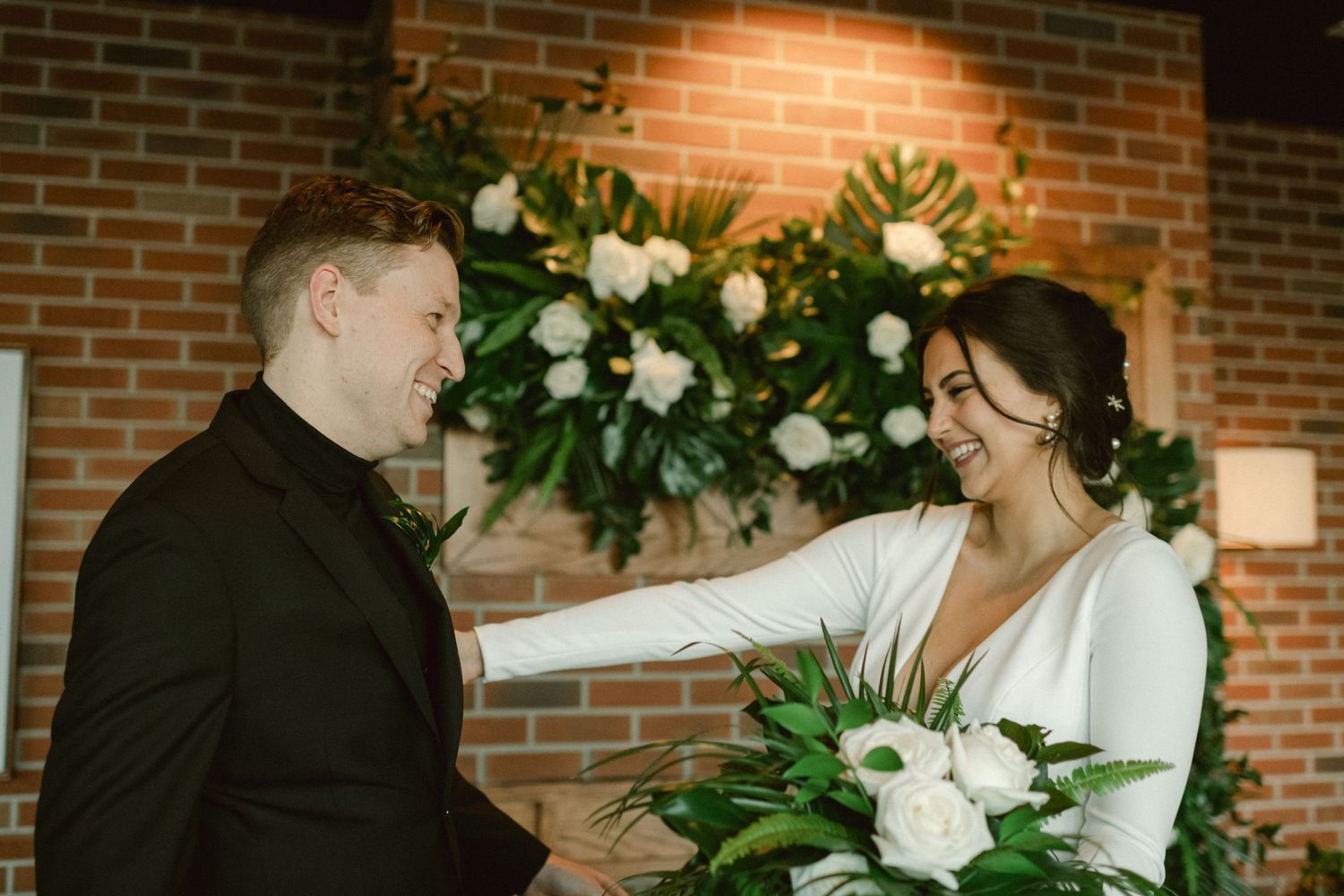 Joyful wedding moment captured in front of white floral wall decoration.