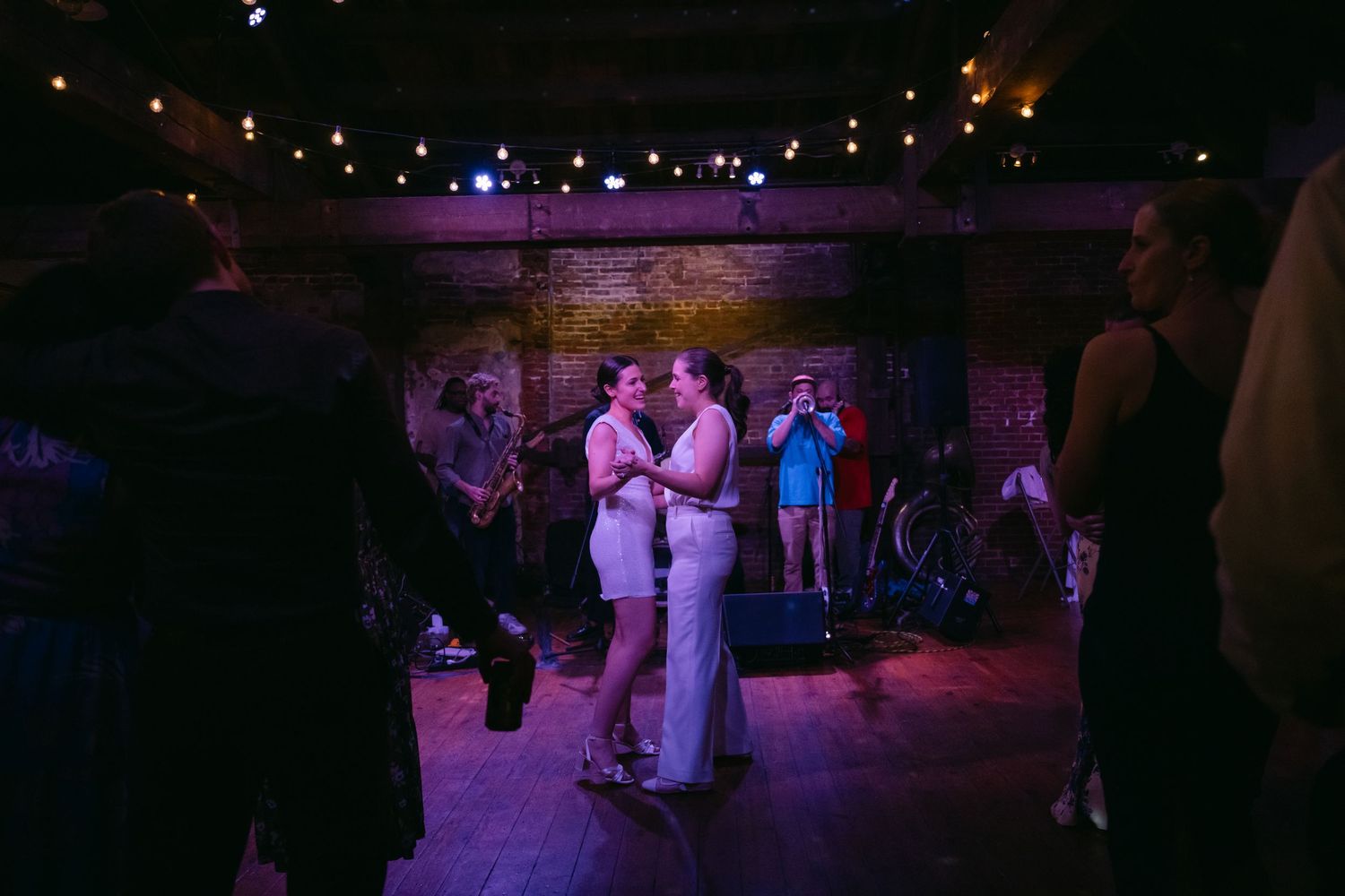 People dancing at a dimly lit wedding reception party with purple lighting and décor creating an elegant atmosphere.
